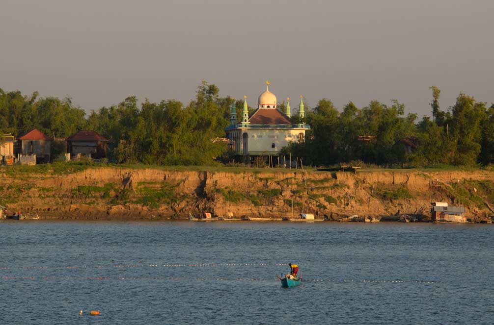 A mosque lit up by the lat afternoon sun. A fisherman tends his nets in the river