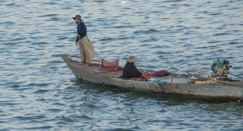 A woman stands on the bow of a simple fishing boat hand fishing