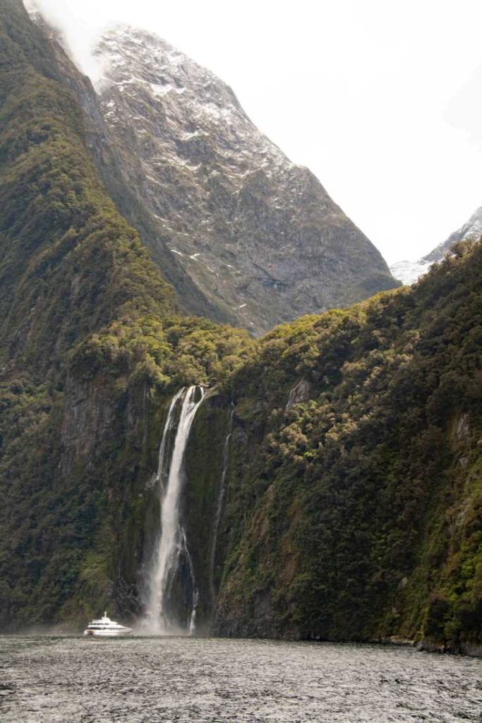 A cruise boat sits at the base of a huge waterfall spilling into the sound