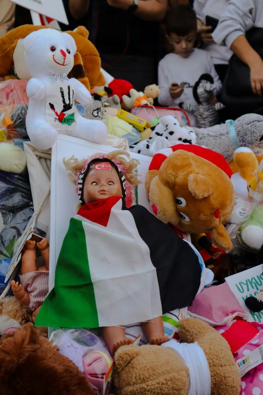 Children's toys in a pile dominated by a doll draped in a Palestinian flag