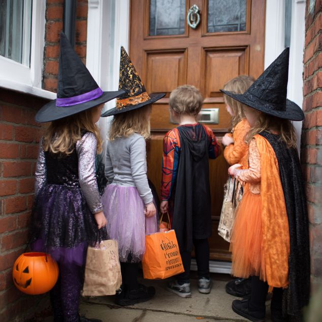 Halloween kids in costumes standing at a door for trick or treat